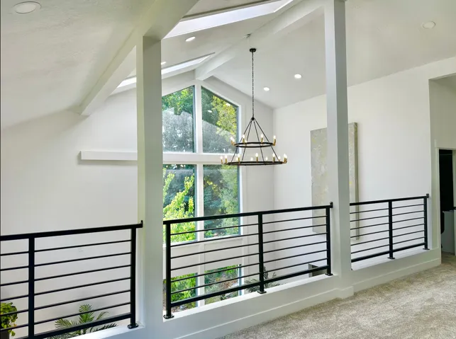 Vaulted ceilings with skylights, expansive window wall, modern black horizontal railing, recessed lighting, and a tiered chandelier