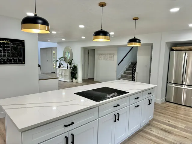 Kitchen island featuring a built-in cooktop, white cabinetry with matte black hardware, and a white countertop with gray veining