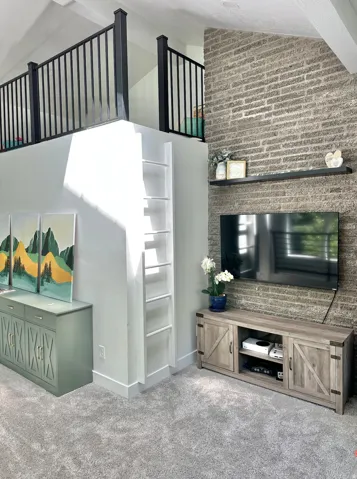 Interior space featuring an upper loft area with black metal railing, a ladder for access, and a prominent brick-finish accent wall
