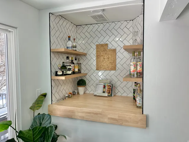 Recessed niche bar featuring herringbone subway tile, wood-finish floating shelves, and a butcher block countertop