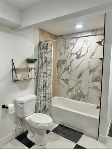 Bathroom featuring a shower/tub combination with large-format marble-look wall tiles, a white porcelain toilet, and a black and white checkerboard floor