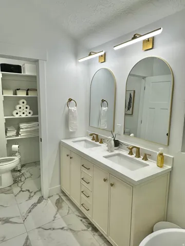 Double vanity featuring cream-colored cabinetry with gold-toned hardware, dual undermount sinks, and a white countertop