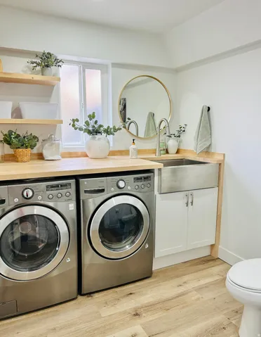 Laundry area featuring wood-finish flooring, light wood countertops, and a stainless steel farmhouse-style sink