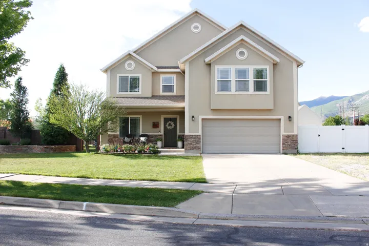 Two-story stucco exterior featuring stone accents, a two-car garage, a concrete driveway, RV parking a manicured lawn, and mature landscaping