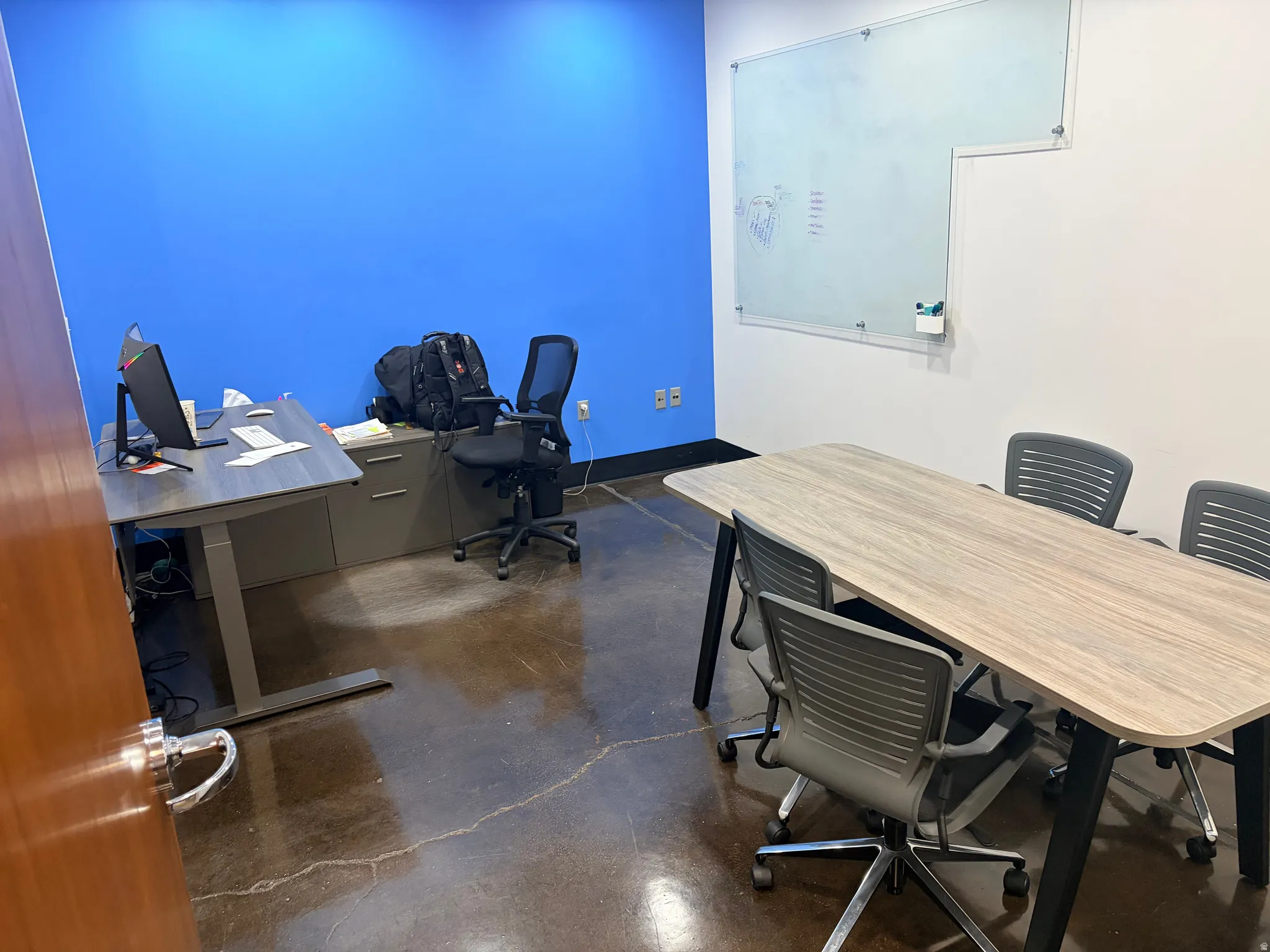 Polished concrete flooring, feature wall with vibrant blue paint, white painted walls, and a wall-mounted glass dry-erase board