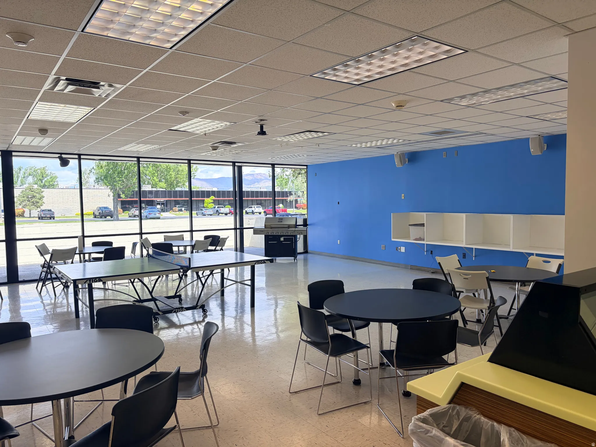 Spacious communal area featuring extensive window lines, a drop ceiling with recessed lighting, and a vibrant blue accent wall