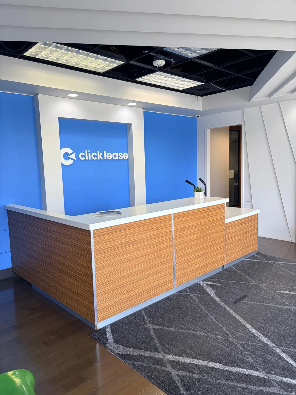 Reception area featuring a wood-finish desk with white countertop, recessed lighting, and a modern gray area rug with geometric patterns
