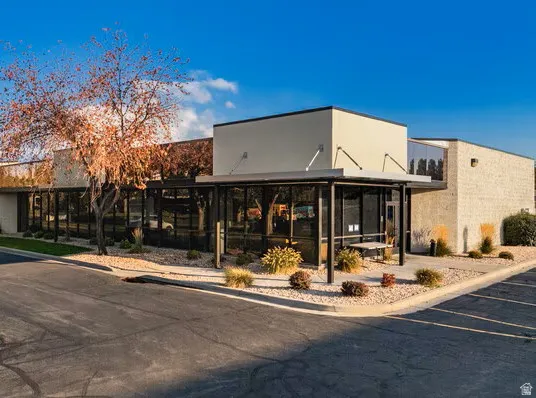 Commercial building with a tan stucco facade, expansive glass storefront windows, a covered entrance, and an asphalt parking area