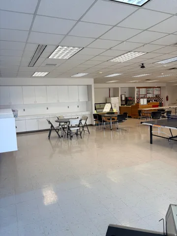 Spacious interior featuring a grid ceiling with integrated fluorescent lighting, extensive built-in white cabinetry, a light-toned tile floor, a built-in counter space, and a serving area with display shelving