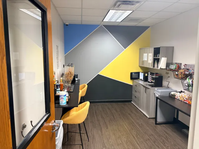 Functional breakroom with wood-finish flooring, geometric accent wall, and built-in cabinetry