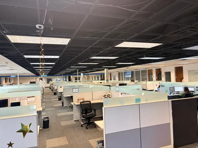 Open-plan office space featuring a suspended ceiling grid with integrated fluorescent lighting panels