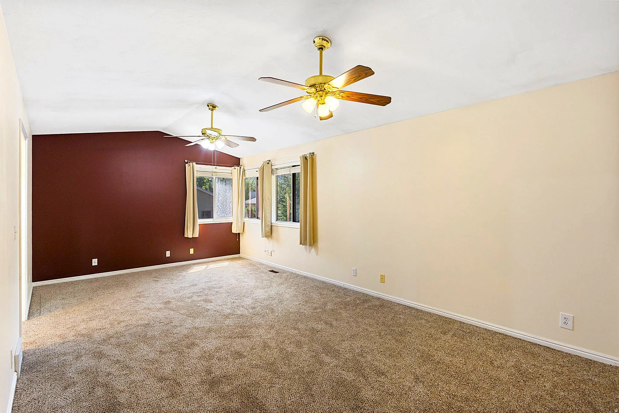 Primary Suite, spacious room featuring vaulted ceilings, two ceiling fans with integrated lighting, two windows, and neutral carpet flooring