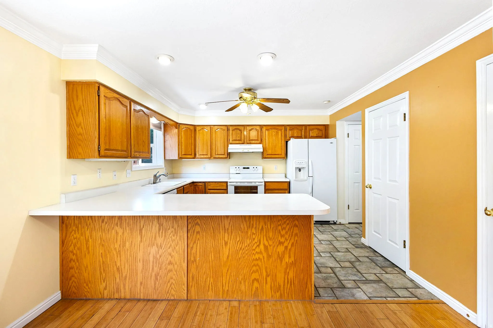 Kitchen featuring wood-finish cabinetry, white countertops, and white appliances, with tile floor.