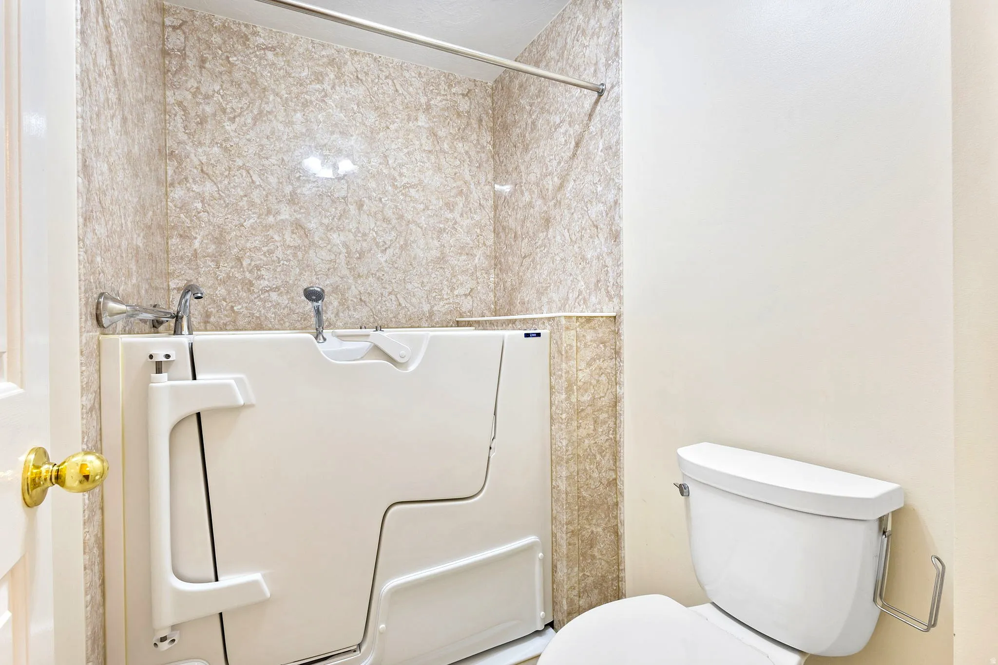 Primary bathroom featuring a walk-in tub with a grab bar, wall-mounted faucet, and shower head, surrounded by decorative wall panels