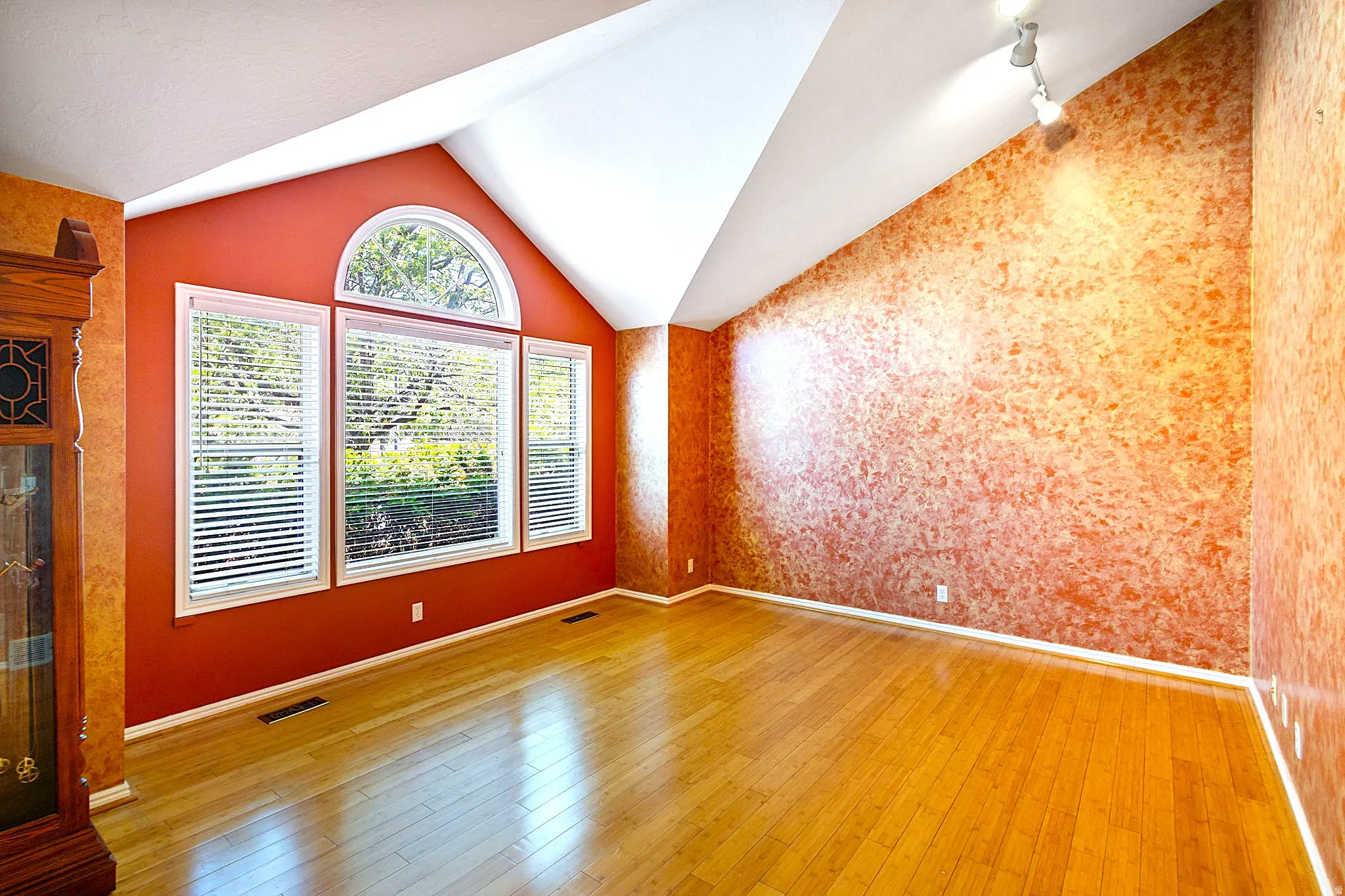Spacious room featuring vaulted ceilings, wood-finish flooring, and a large window array with an arched transom