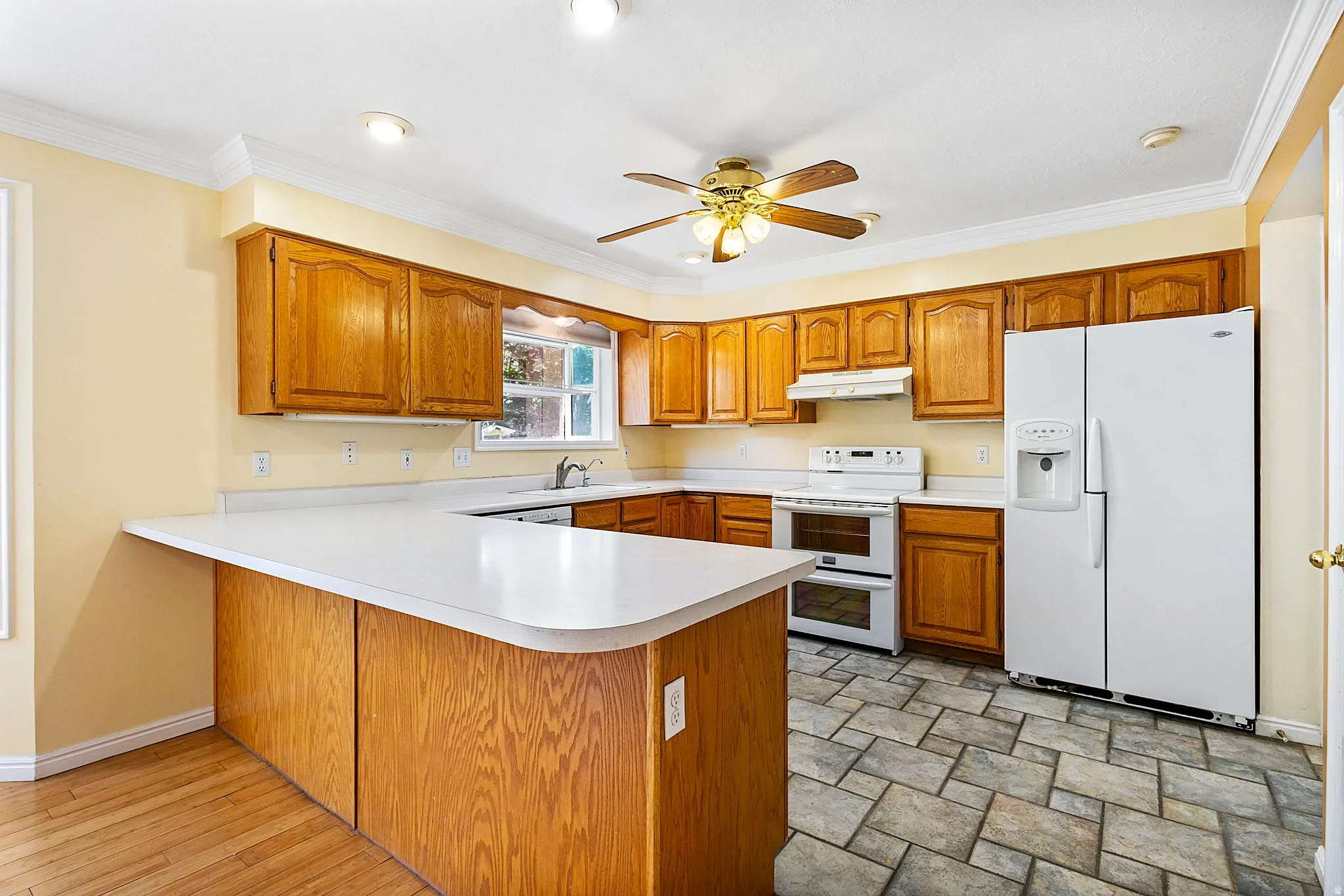 U-shaped kitchen featuring wood cabinetry, white countertops, and a ceiling fan with integrated lighting and tile floor.