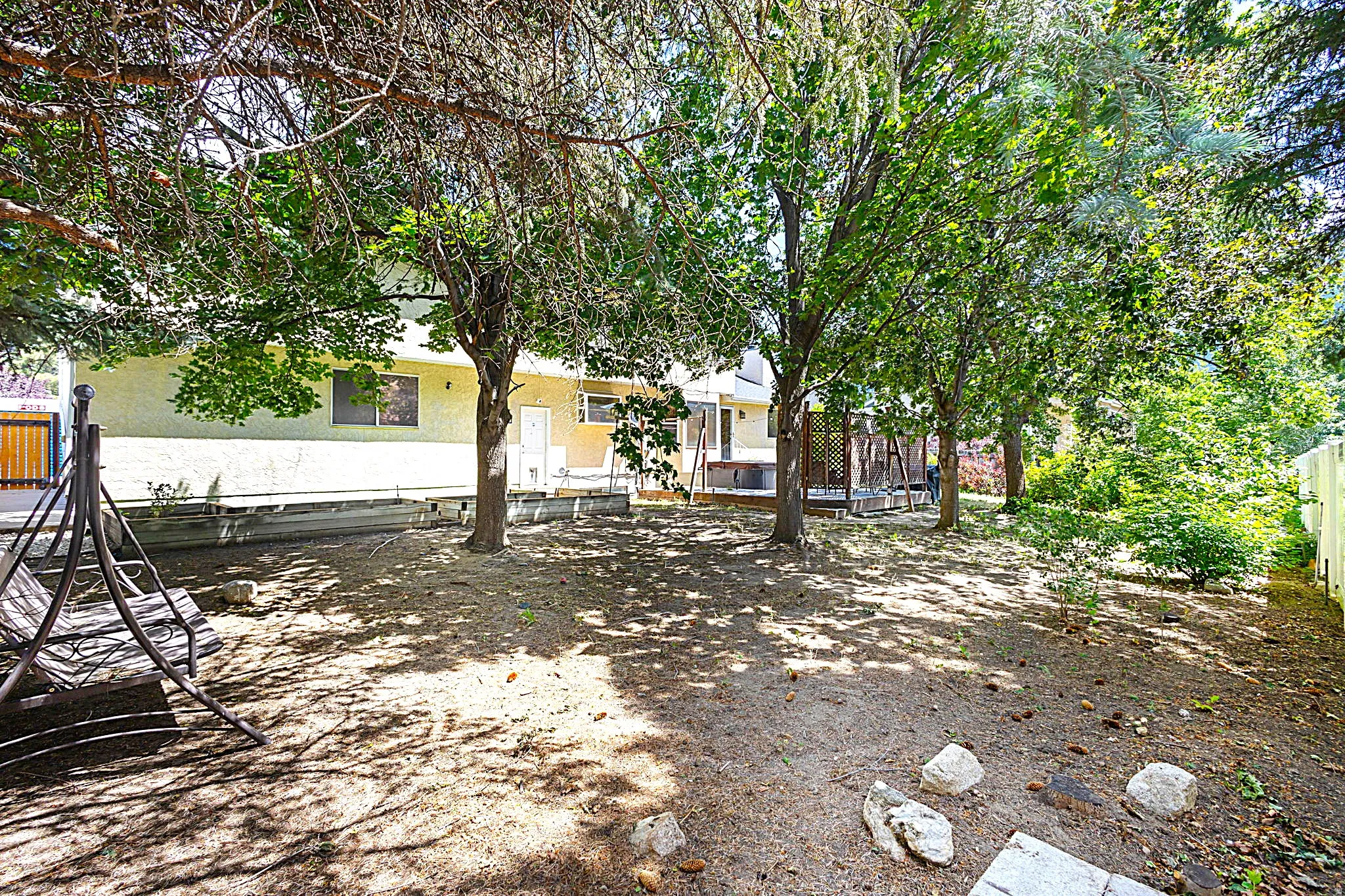 Expansive backyard featuring mature trees providing natural shade, a large wooden deck, and a stucco exterior