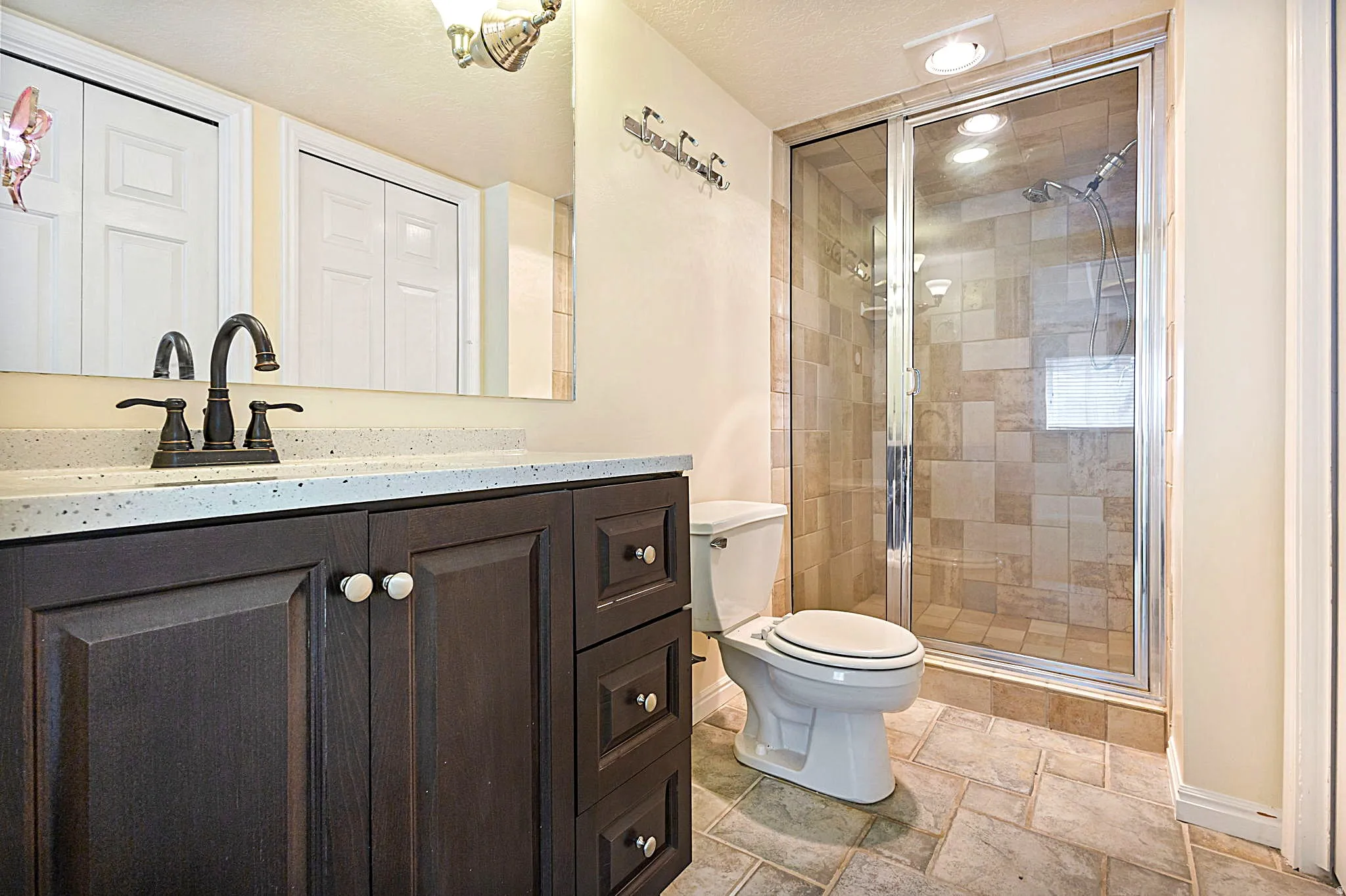Bathroom featuring a dark wood-finish vanity with a light speckled quartz countertop, bronze-finish faucet, and a large mirror