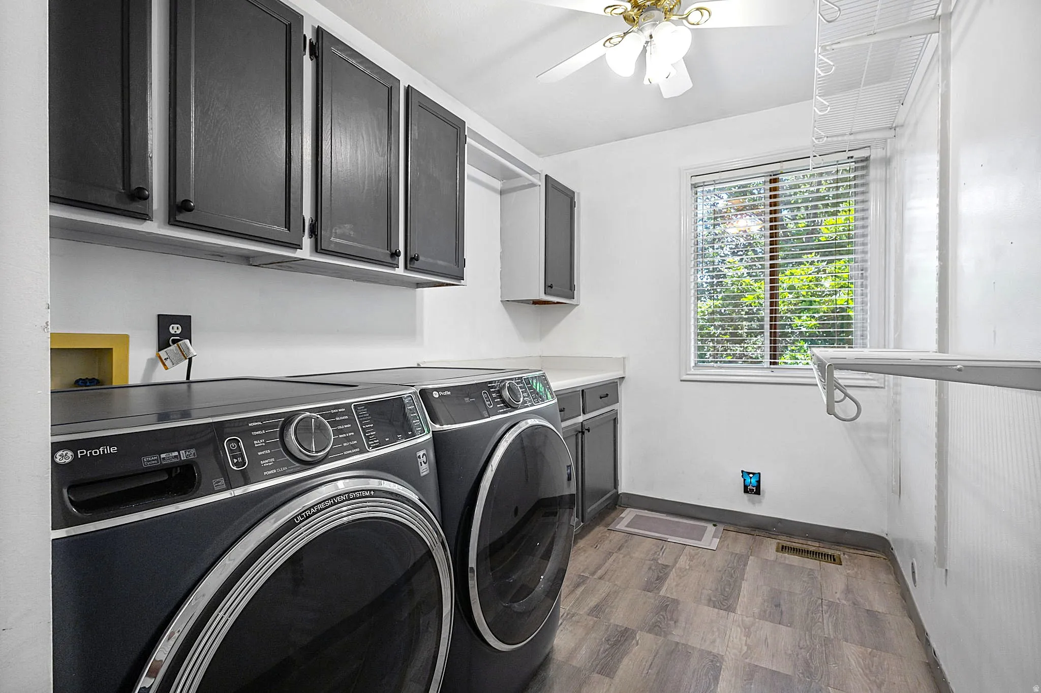 Dedicated laundry space featuring dark cabinetry, wood-finish flooring, and a window with natural light