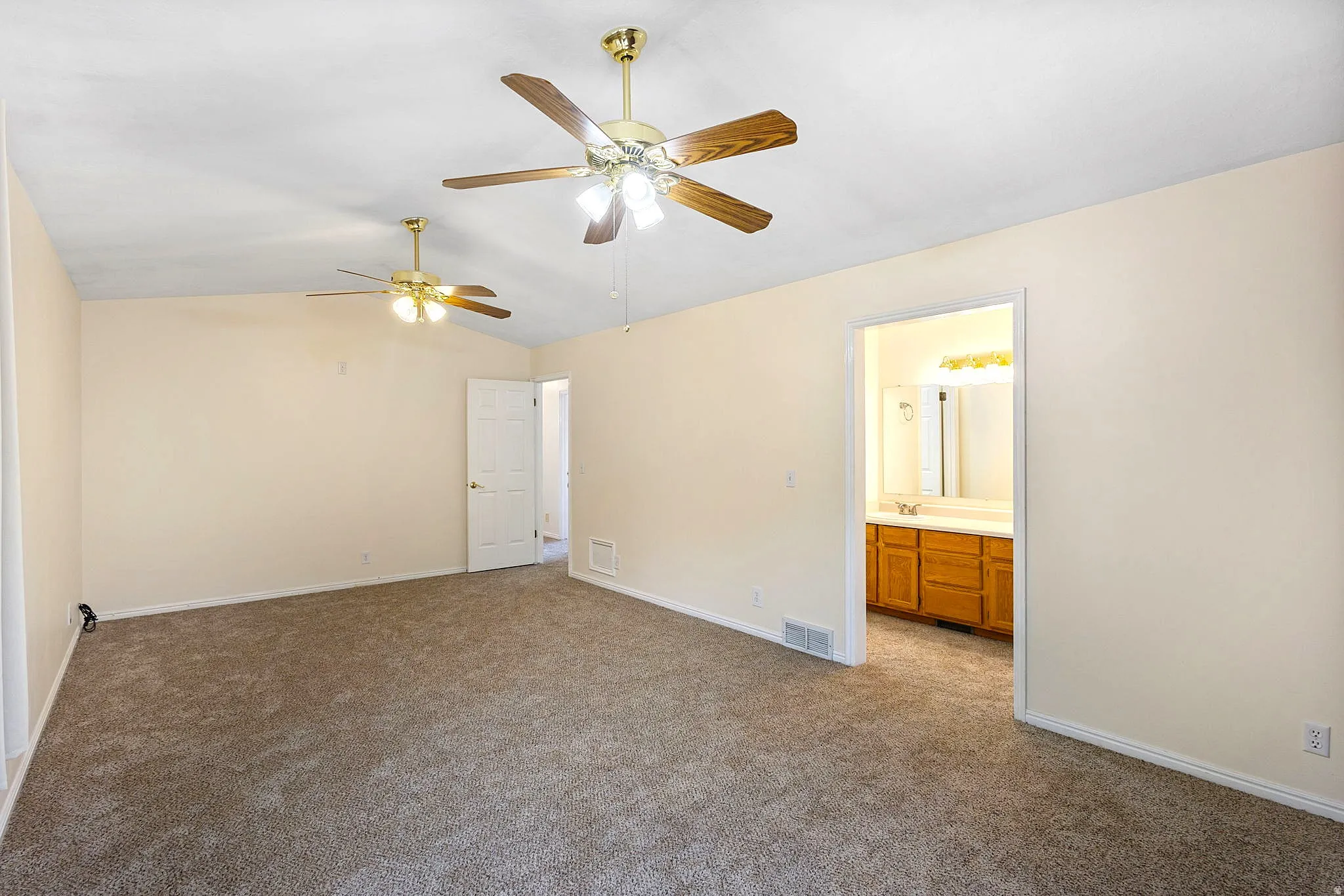 Primary Suite, spacious room featuring vaulted ceilings, two ceiling fans with light kits, and carpet flooring