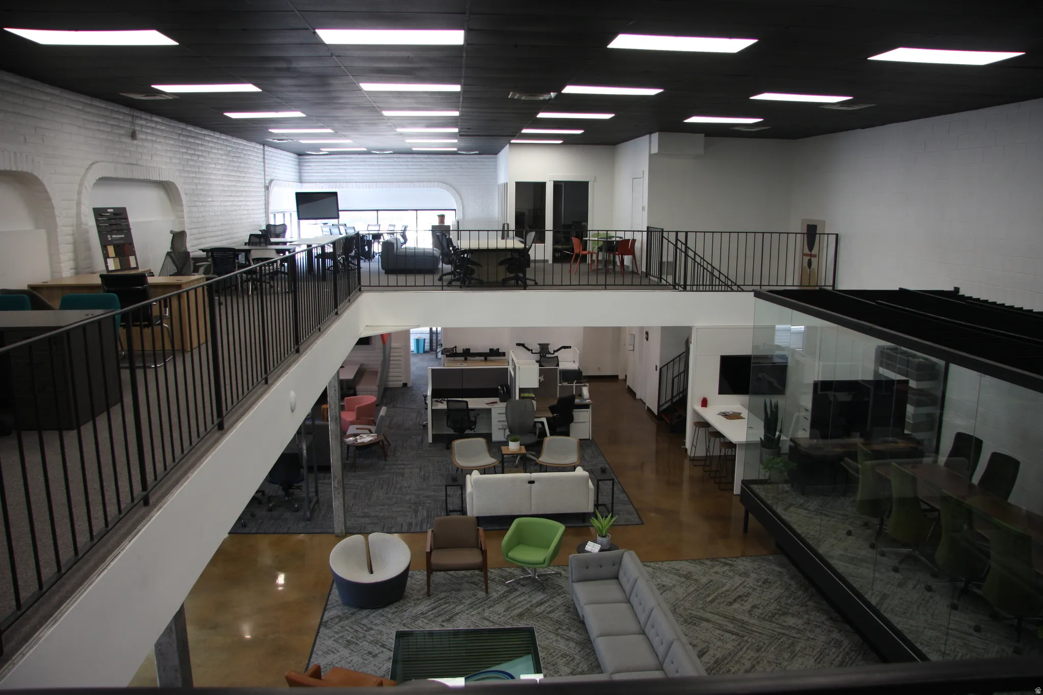 Spacious multi-level commercial interior featuring a mezzanine overlook with metal railings, a conference room with glass walls, and recessed lighting fixtures