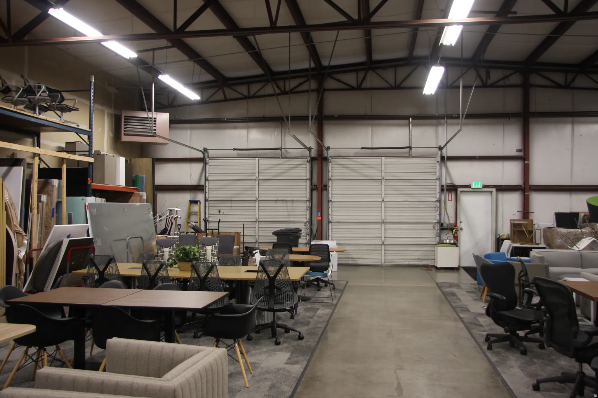 Spacious warehouse interior featuring high ceilings with exposed metal trusses and overhead fluorescent lighting