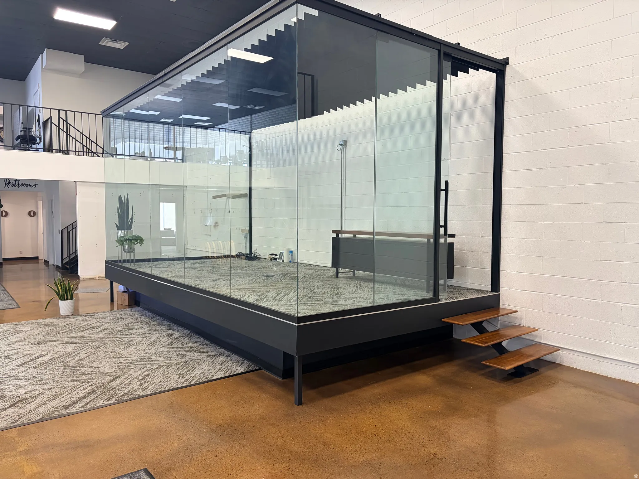 Glass-enclosed elevated platform featuring a black metal frame, integrated wood-finish steps, and a sliding glass door