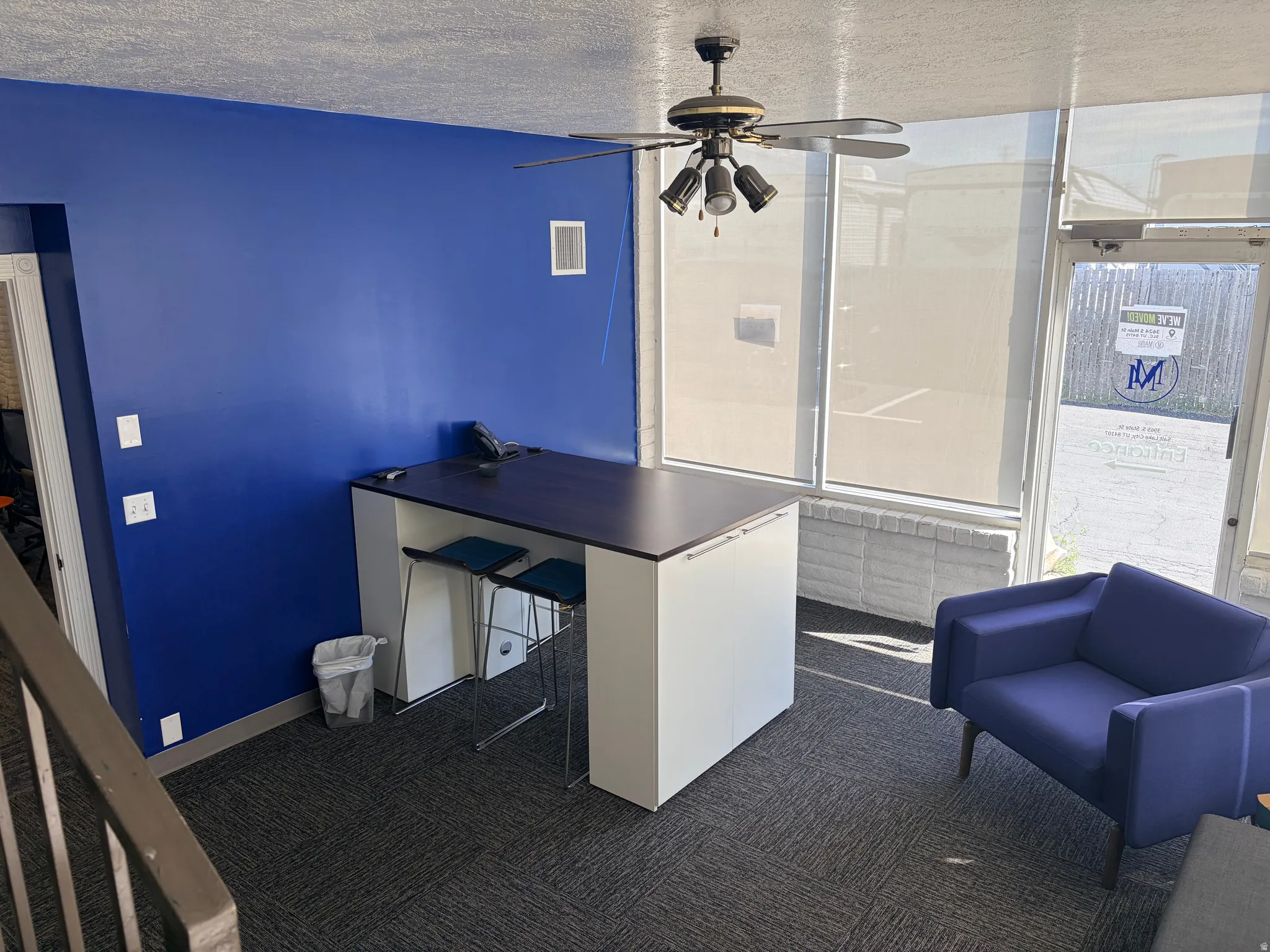 Interior space featuring a built-in counter-height desk, a ceiling fan with integrated lighting, and large windows with roller shades