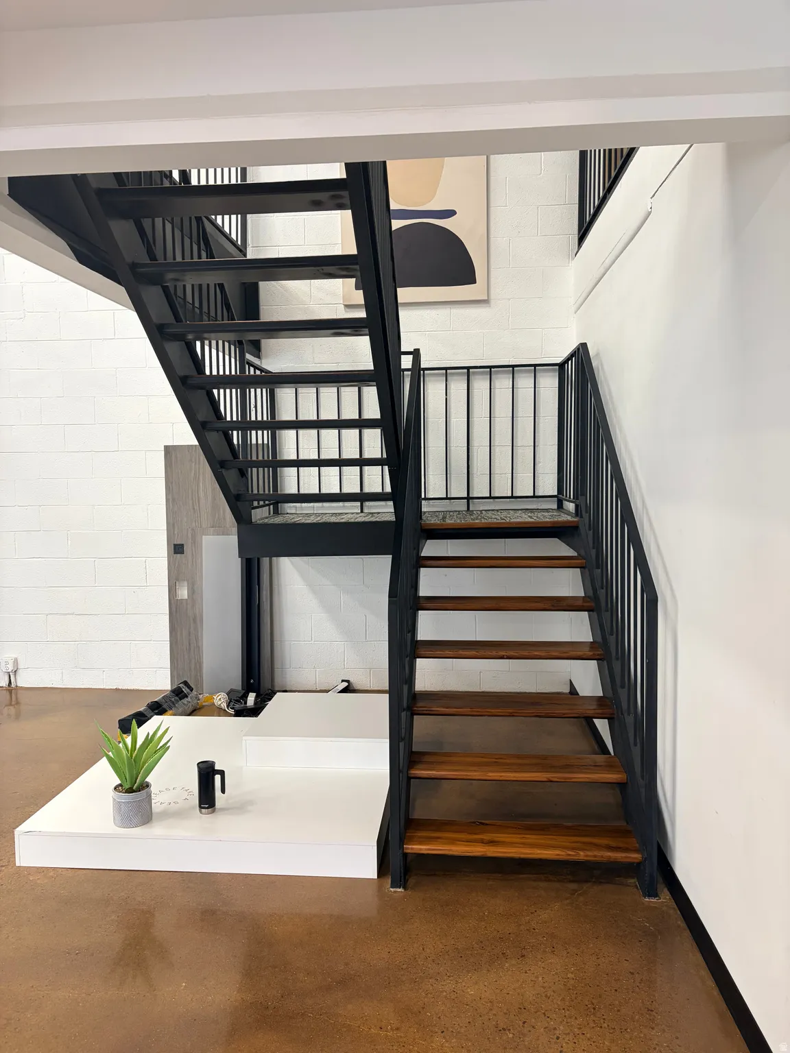 Industrial-style metal staircase with wood-finish treads, concrete flooring, and white block wall construction
