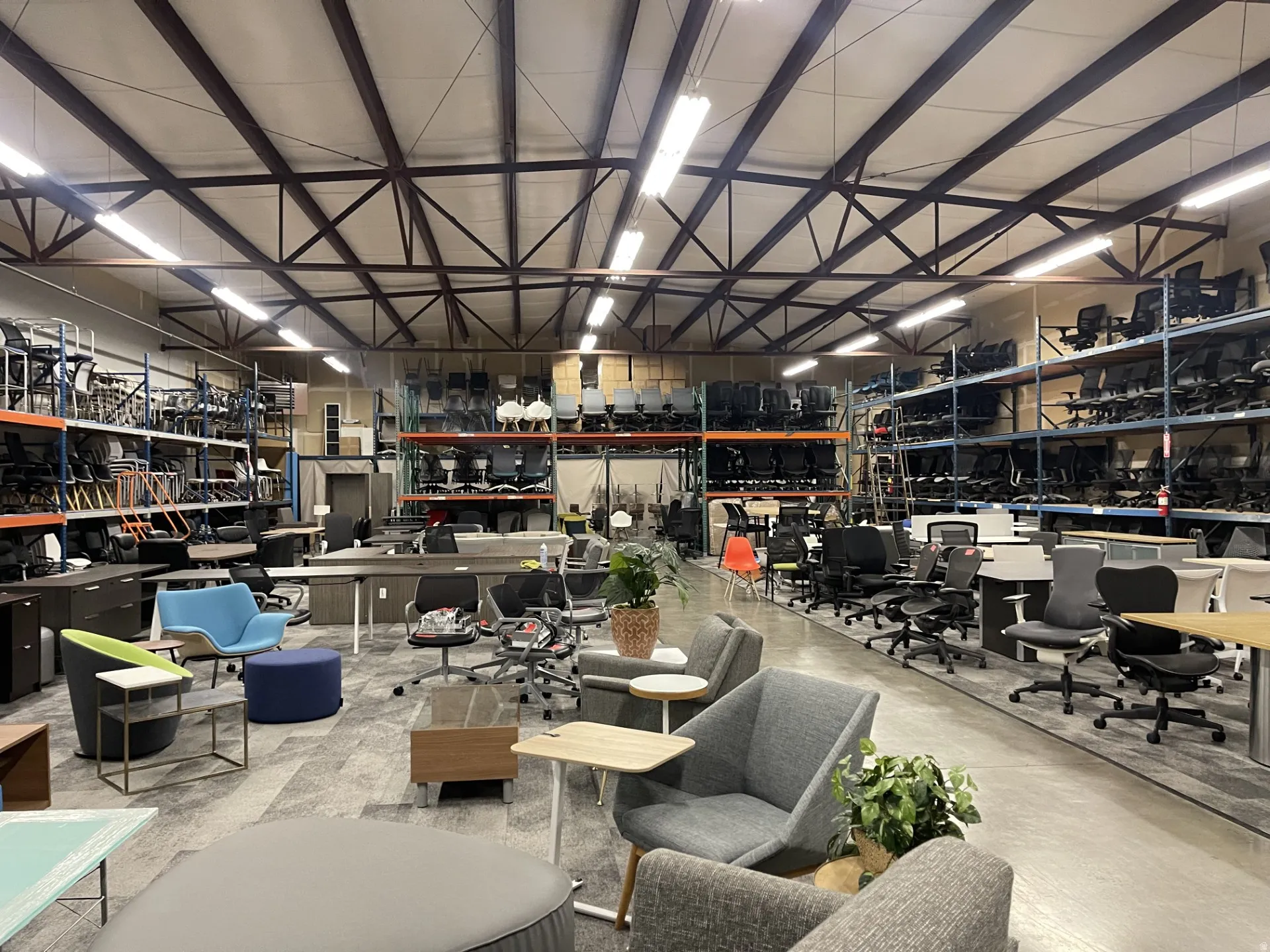 High-ceiling warehouse featuring exposed steel trusses, extensive shelving systems, and concrete flooring