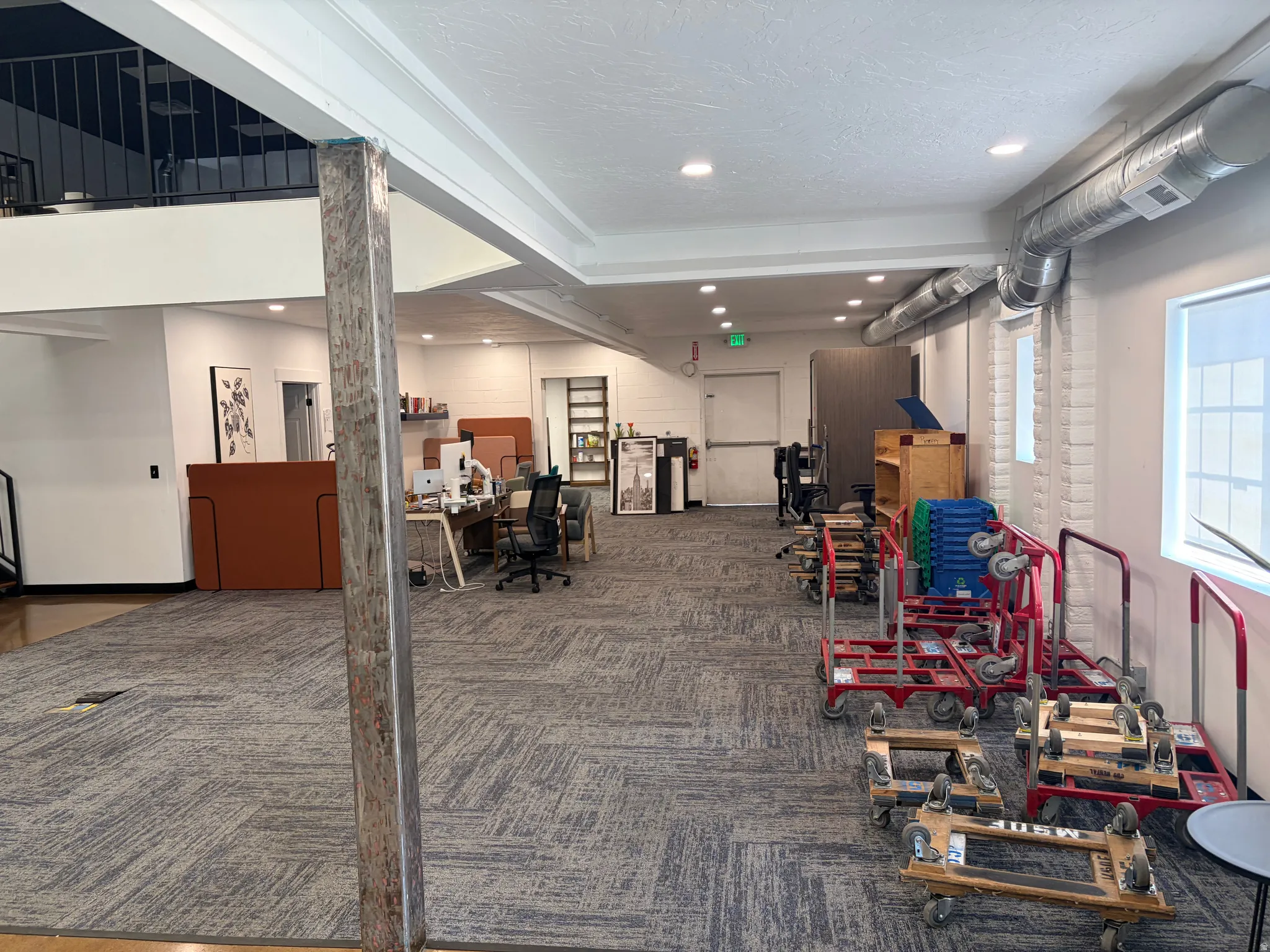 Spacious open-concept interior featuring patterned carpet flooring and a partial second-story overlook with a metal railing