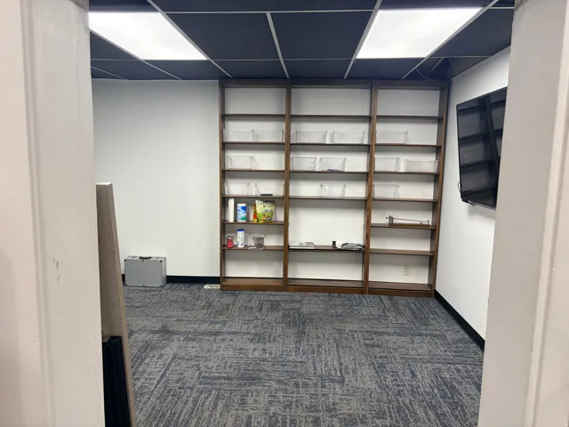 Room featuring dark wood-finish built-in shelving, patterned carpet flooring, and a suspended ceiling with integrated lighting panels