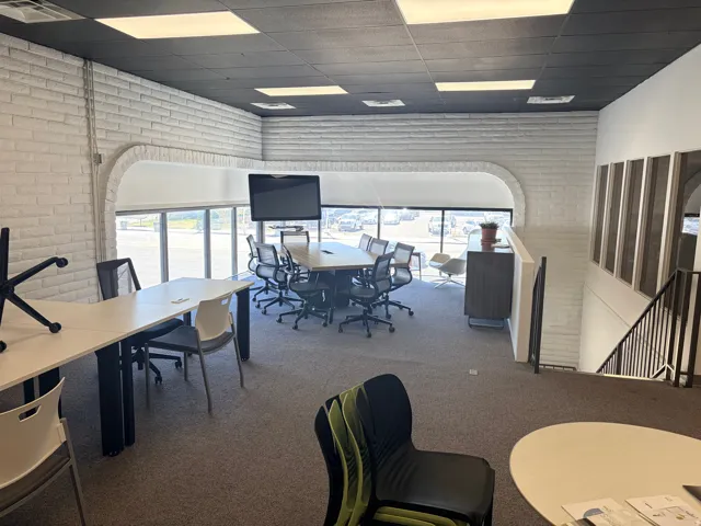 Open-concept workspace featuring white painted brick walls and broad windows with roller shades