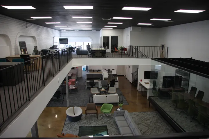 Spacious multi-level commercial interior featuring a mezzanine overlook with metal railings, a conference room with glass walls, and recessed lighting fixtures