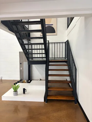 Industrial-style metal staircase with wood-finish treads, concrete flooring, and white block wall construction