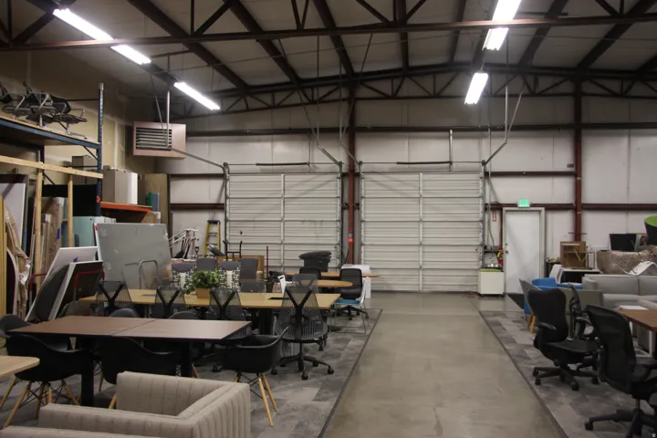 Spacious warehouse interior featuring high ceilings with exposed metal trusses and overhead fluorescent lighting