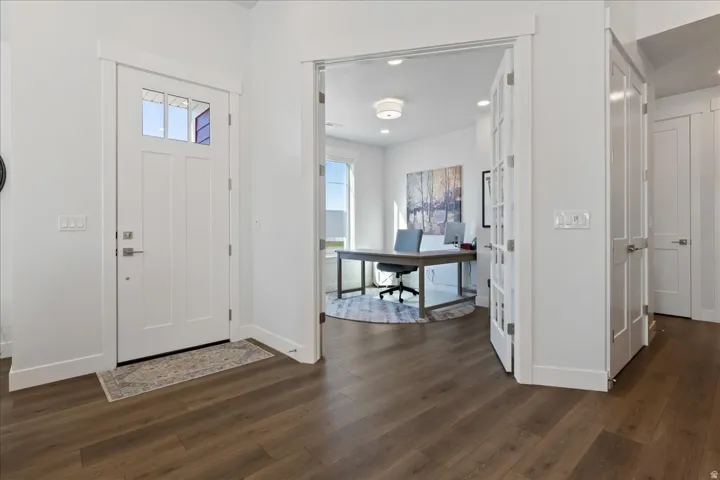 Entryway featuring wood-finish flooring, a white paneled entry door with clear glass lites, a bright white interior, and a recessed office space with French doors