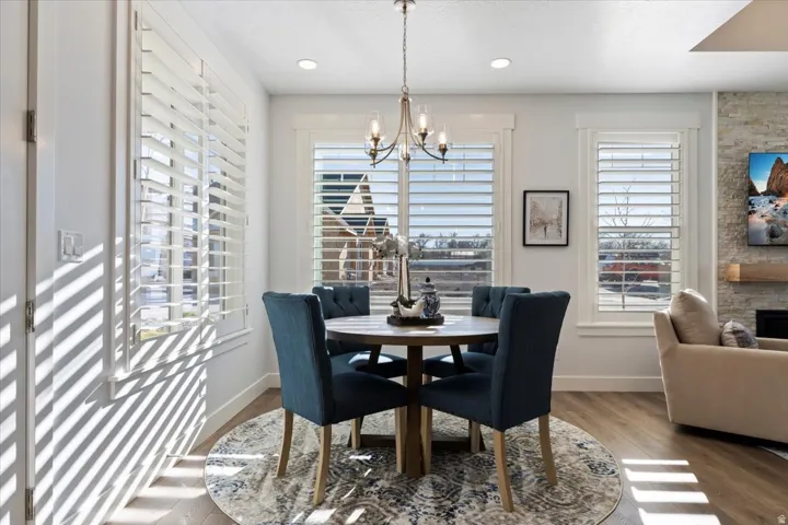 Dining area featuring wood-finish flooring, a contemporary chandelier, and multiple windows with white plantation shutters
