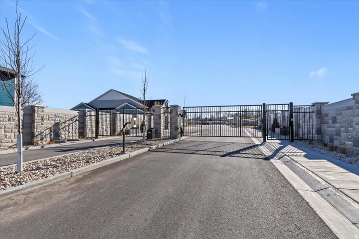 Gated entry featuring black wrought iron gates, stone masonry pillars, and a stone masonry perimeter wall