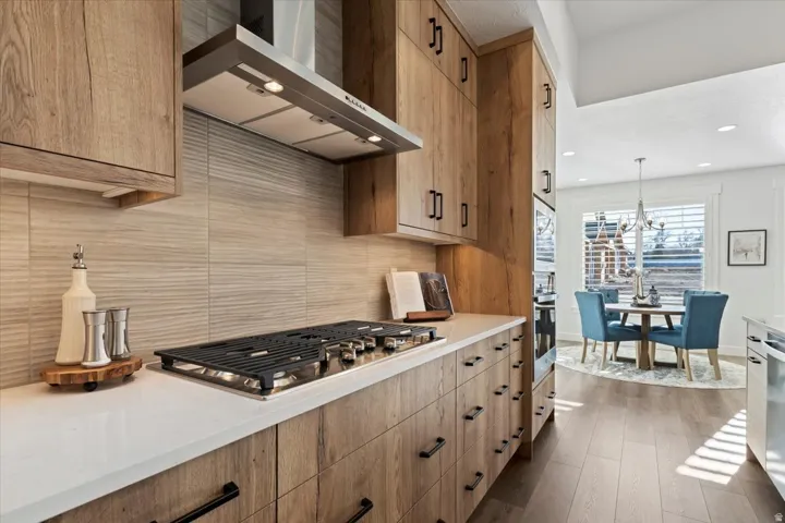 Modern kitchen featuring light wood-finish cabinetry with black hardware, white countertops, and a stainless steel range hood