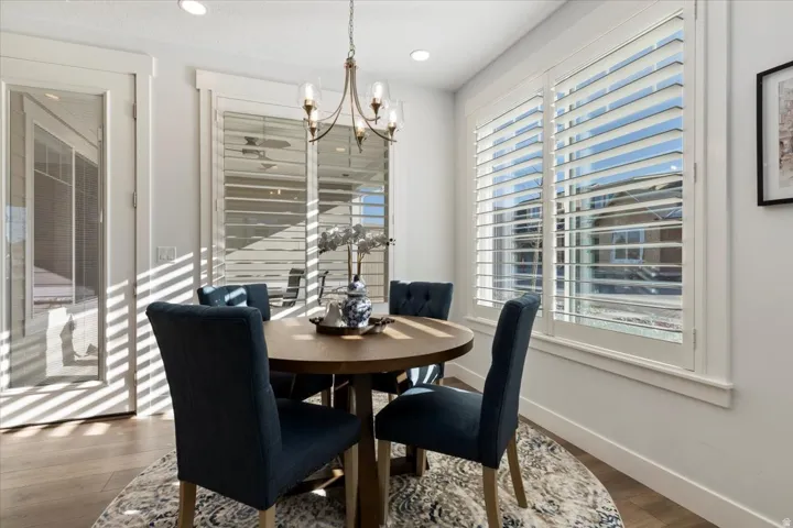 Dining area featuring wood-finish flooring, white plantation shutters, a glass-paneled door, recessed lighting, and a chandelier with glass shades