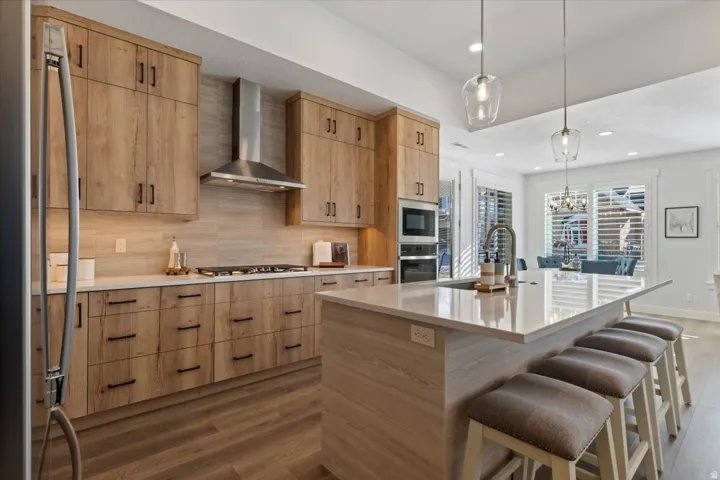 Kitchen featuring wood-finish cabinetry with black hardware, stainless steel appliances, a gas range with a stainless steel hood, and light-toned countertops