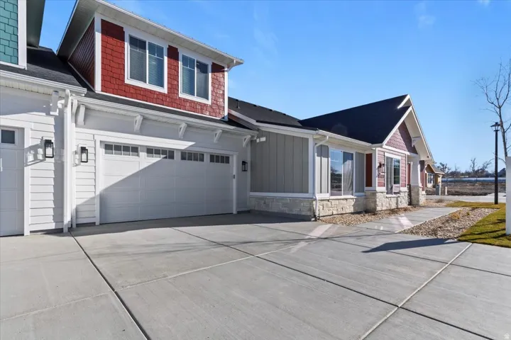 Modern home exterior featuring a two-car garage, white siding, red shingle accents, and a stone facade