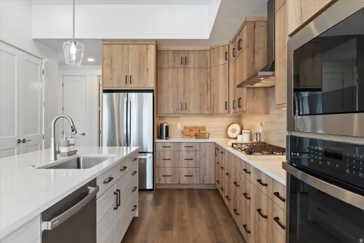 Contemporary kitchen featuring light wood-finish cabinetry, stainless steel appliances, a white countertop, and wood-finish flooring