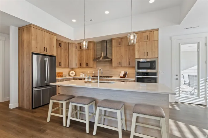 Modern kitchen featuring light wood-finish cabinetry, stainless steel appliances, a center island with countertop seating, recessed lighting, and pendant fixtures