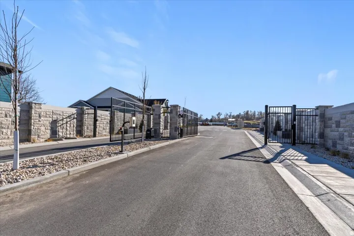 Gated entrance featuring decorative stone walls, black wrought iron gates, asphalt paving, and gravel landscaping