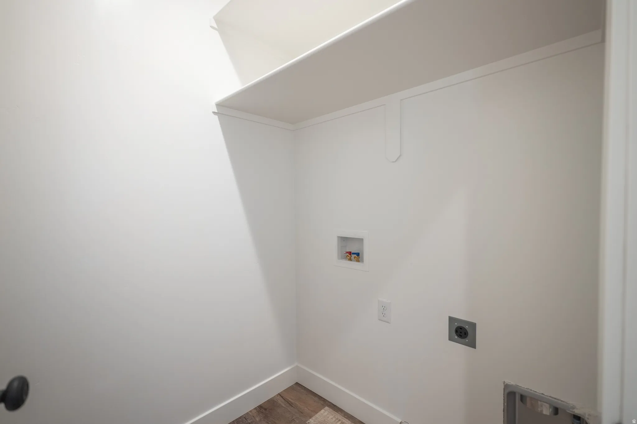 Dedicated utility space featuring a built-in white shelf, white wall finishes, wood-finish flooring, and essential appliance hookups