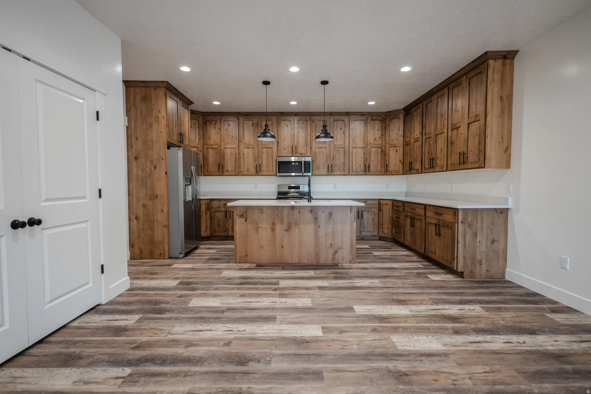 Kitchen featuring wood-finish cabinetry, light countertops, a central island with a sink, stainless steel appliances, and a wood-finish floor