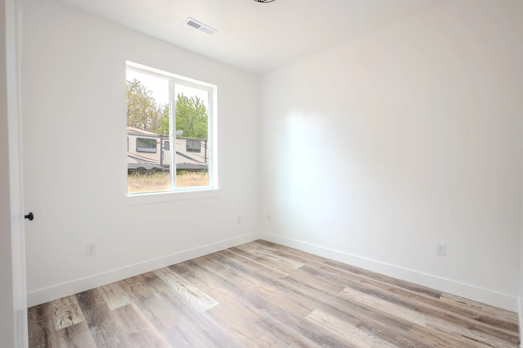 Bright interior space featuring a window, wood-finish flooring, white walls, white baseboards, and a black doorknob