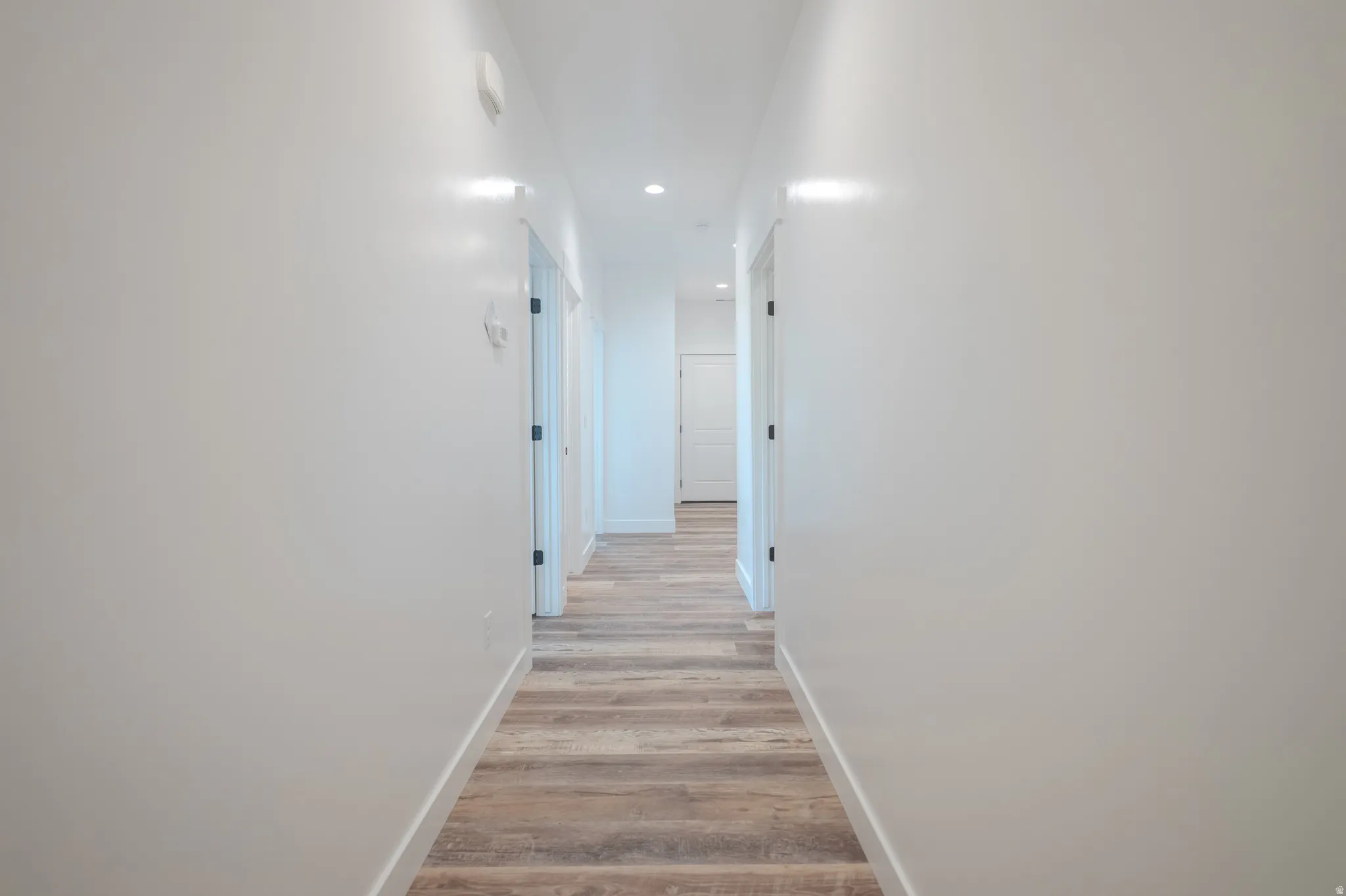 Hallway with wood-finish flooring, recessed lighting, white walls, and multiple panel doors